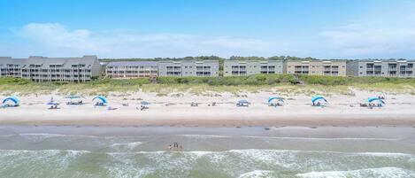 Een strandhotel met meerlaags gebouwen, een zandstrand met parasols en golven op de voorgrond.