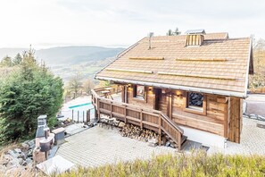A wooden cabin with a deck, a fireplace, and a view of the surrounding landscape.