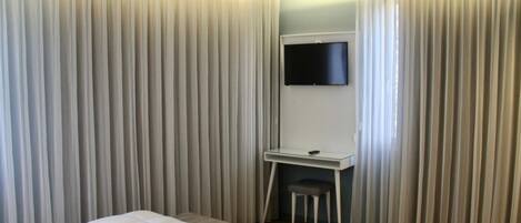 A bedroom with a bed, a desk, and a TV.