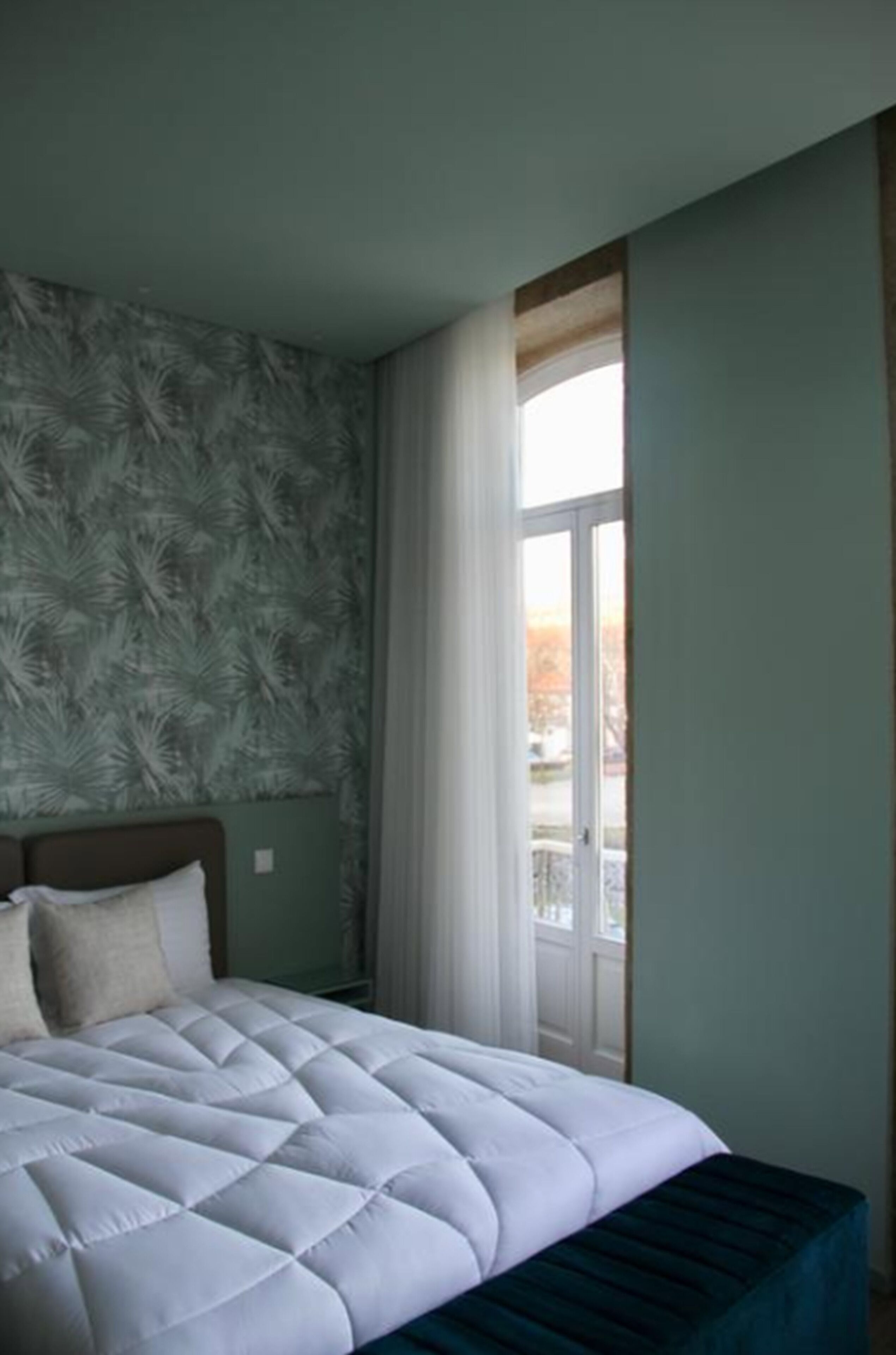 A bedroom with a large bed, a window with curtains, and a view of the outdoors.