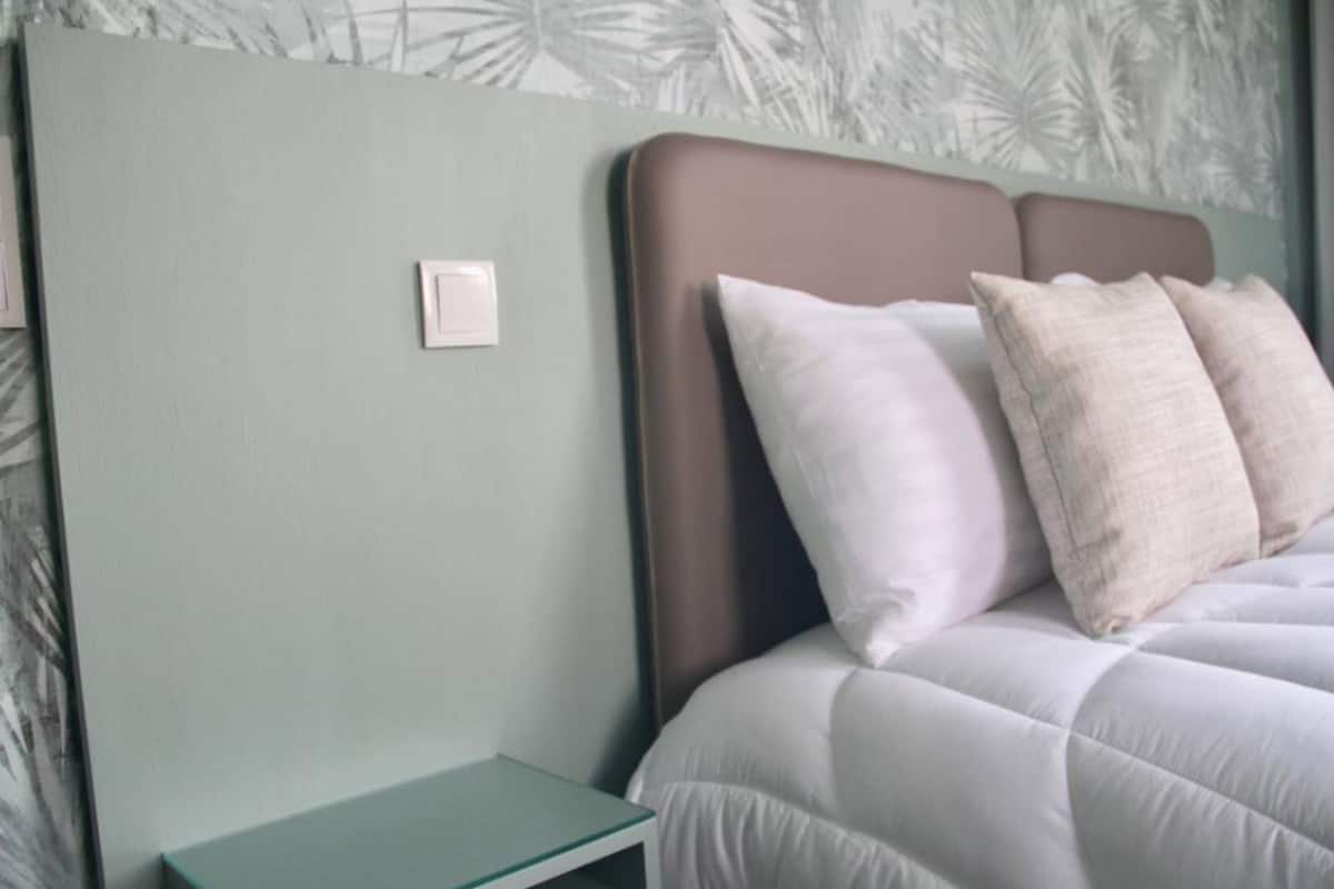 Un lit bien fait, avec une tête de lit, une table de chevet et un mur orné d’un motif végétal.