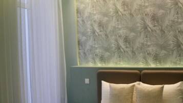 Quarto com cama grande, mesa de cabeceira, luminária na parede e janela com cortinas.