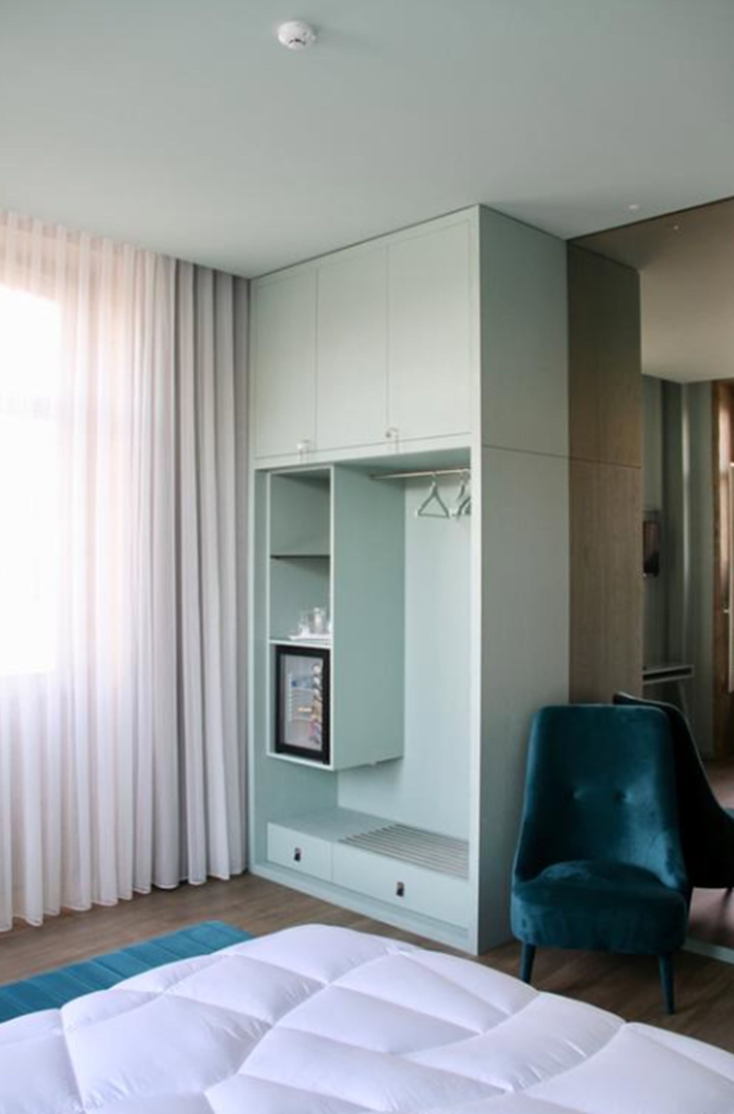 A modern hotel room with a bed, a wardrobe, and a seating area.