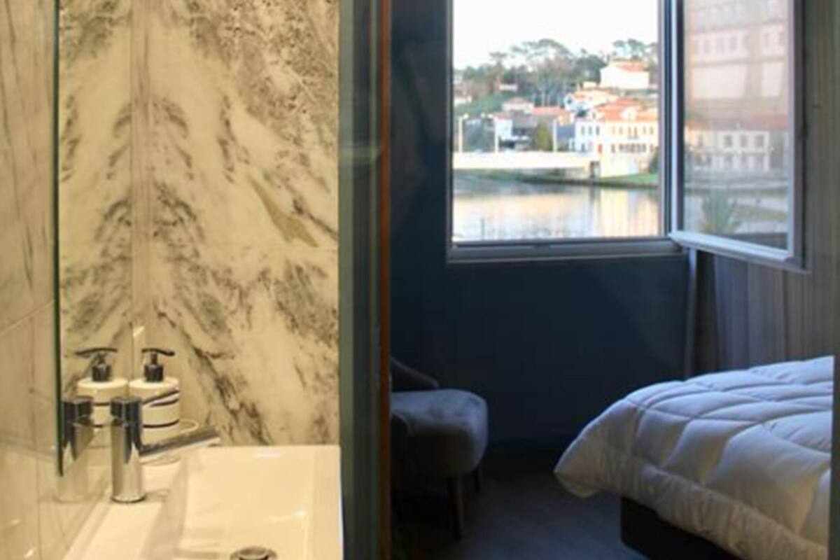 Une salle de bain moderne avec un mur en marbre, un lavabo et une grande fenêtre donnant sur des immeubles et une étendue d’eau.