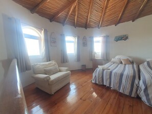 Een kamer met houten vloeren, een bank, een bed met gestreepte lakens en een plafond met houten balken.
