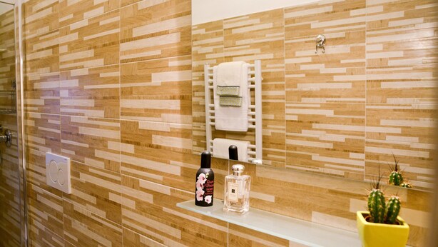 Une salle de bain avec un mur décoré d’une mosaïque en bois, un porte-serviettes blanc, un flacon de parfum, un flacon de lotion et un cactus en pot.