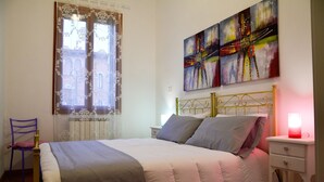 Une chambre à coucher avec un lit, une table de chevet, une chaise et une fenêtre ornée de rideaux en dentelle.