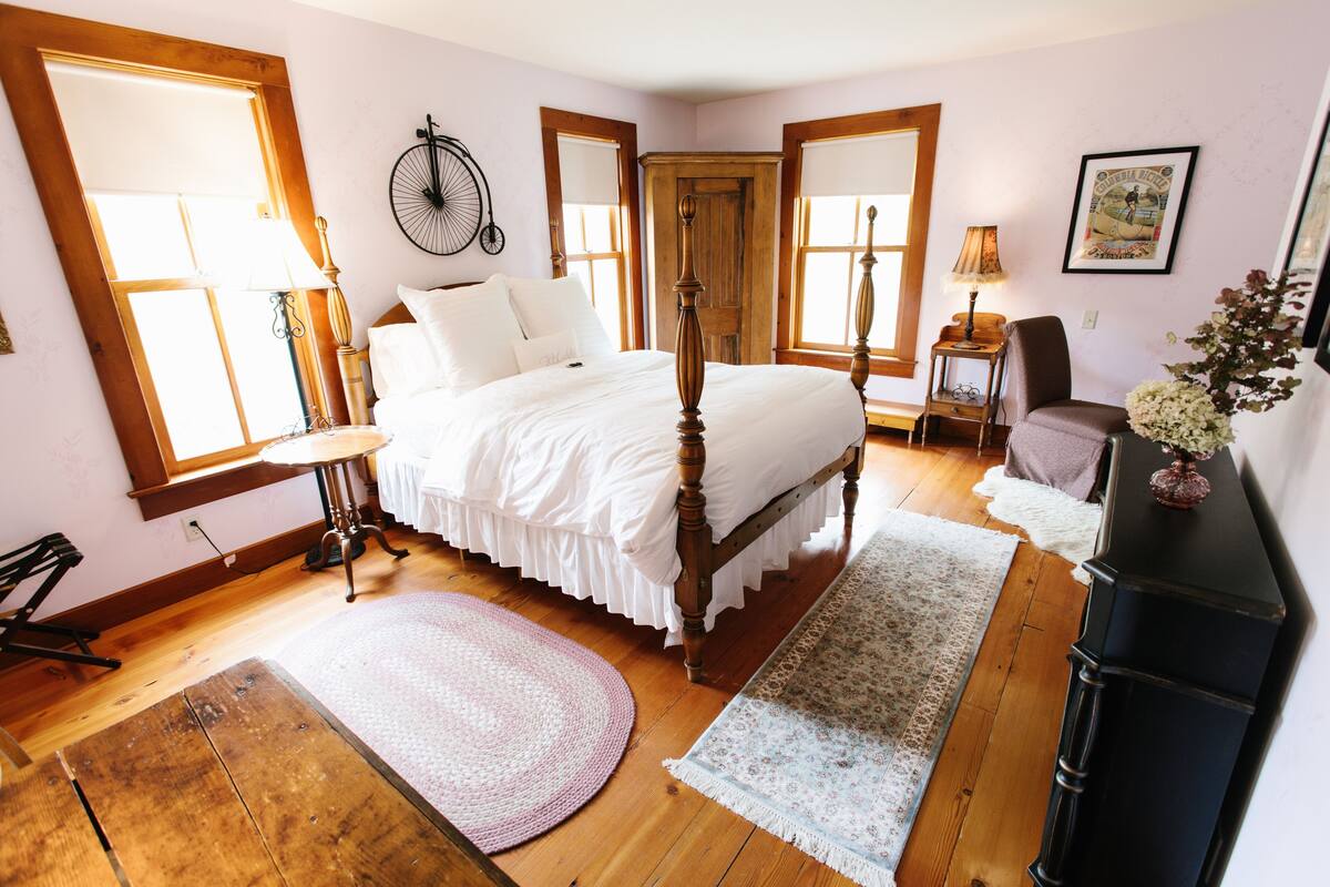 A bedroom with a four-poster bed, wooden flooring, and large windows.