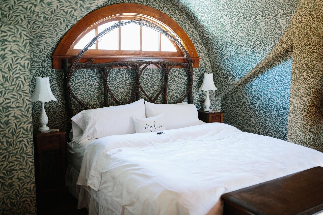 Un dormitorio con cabecera de madera, papel tapiz estampado y cama con ropa blanca.