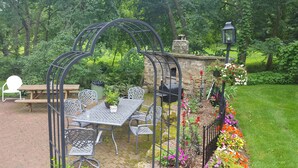 A patio with a table and chairs, a stone wall, and a flower bed. - Round Barn Farm B & B Event Center (Red Wing)