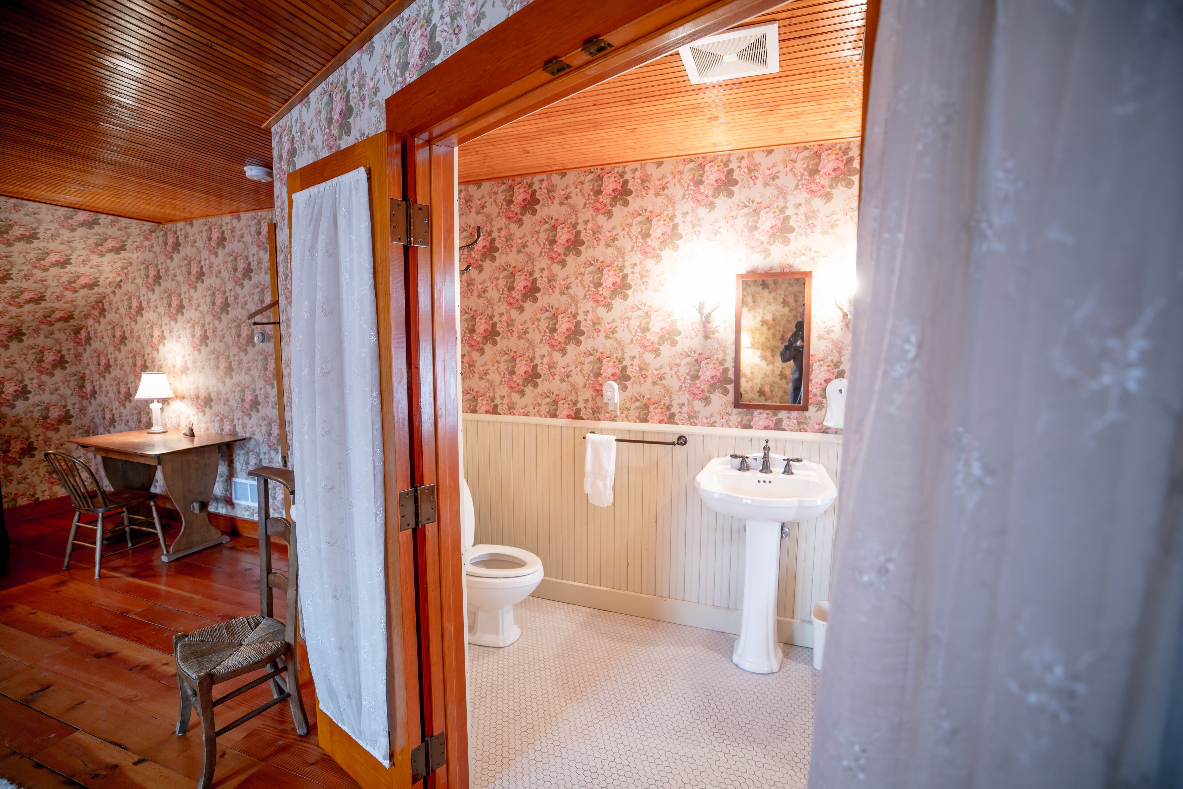 A bathroom with a wooden floor, a toilet, a sink, and a mirror.