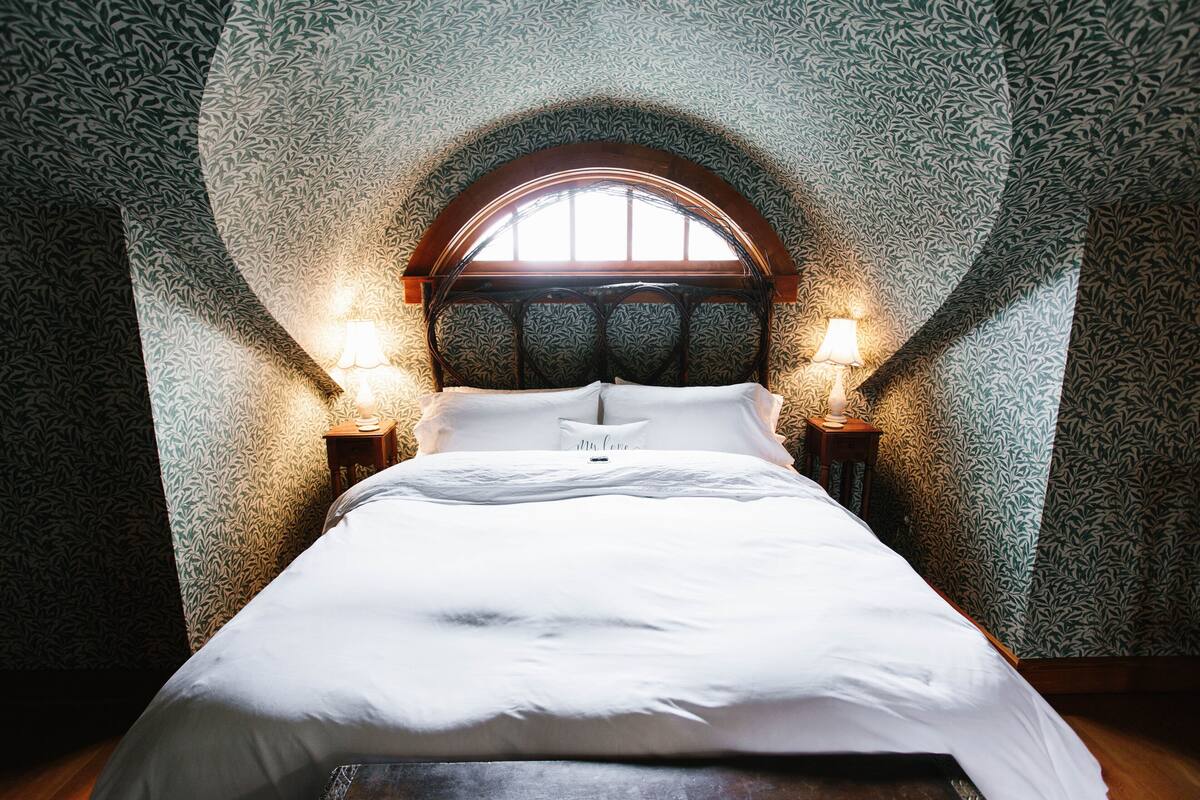 A bedroom with a large bed, two bedside lamps, and a window with a wooden arch.