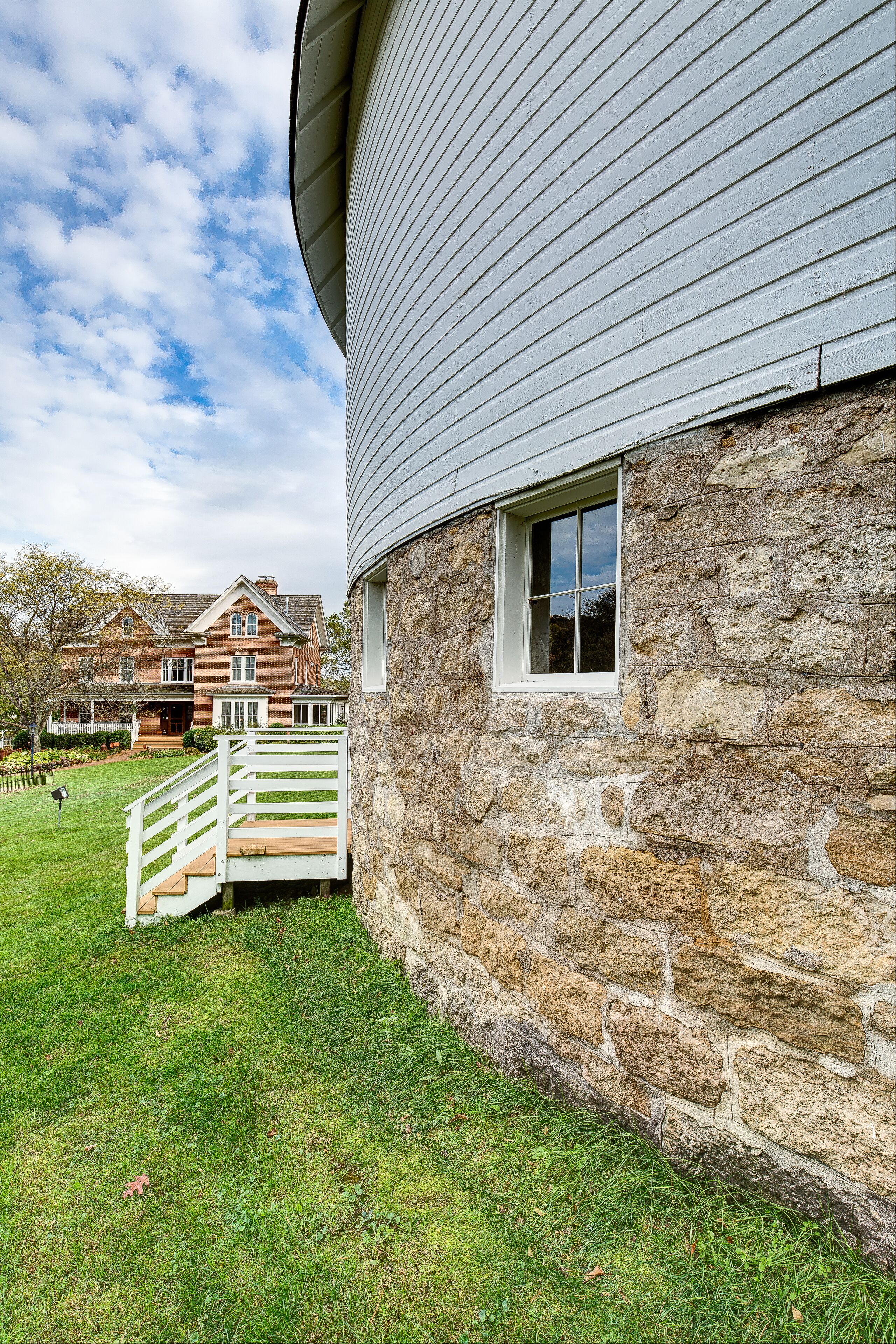 A stone building with a white exterior and a wooden staircase leading to a white door.
