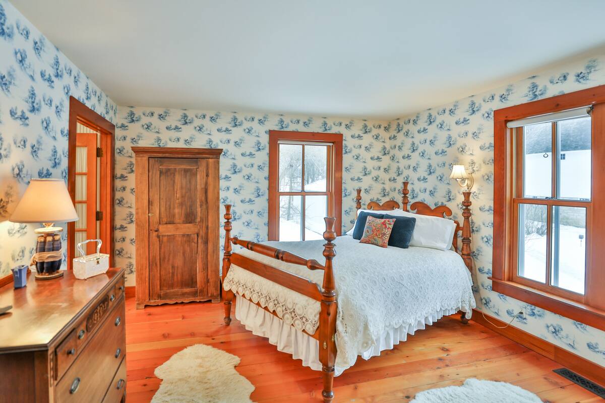 A bedroom with a wooden four-poster bed, a dresser, and a window with a view of the outside.
