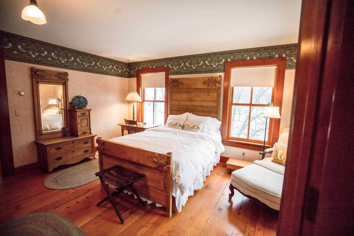 A bedroom with a wooden bed, a dresser, a mirror, and a window with a view.