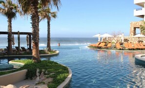 A pool area with lounge chairs and palm trees, overlooking the ocean.