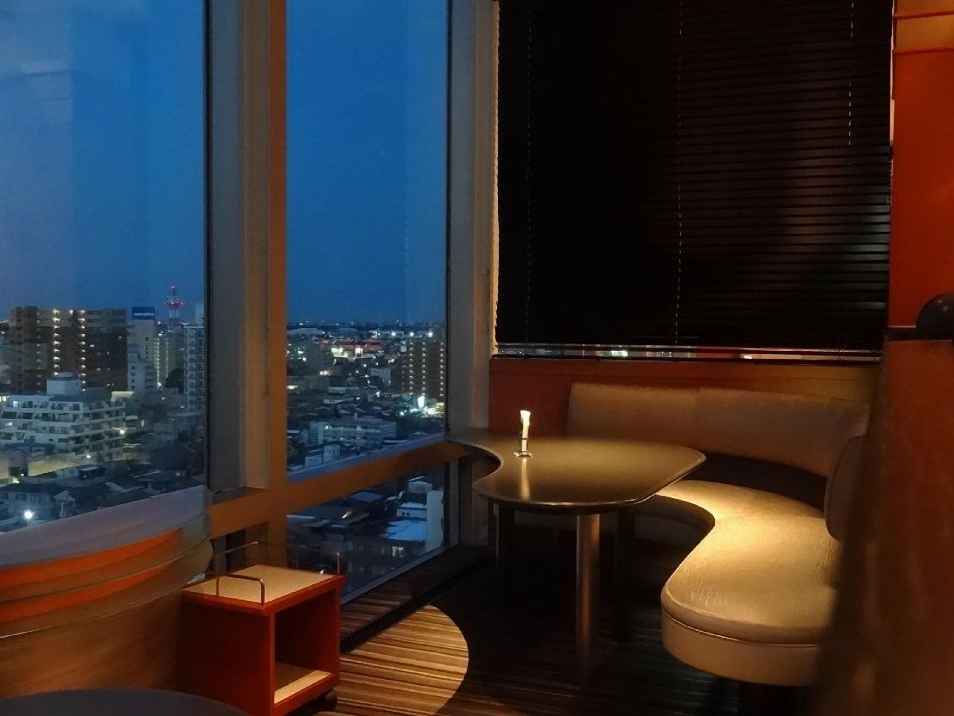 A balcony with a view of a cityscape at night, a round table, and a cushioned seating area.