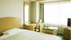 Una habitación de hotel con cama, escritorio, silla, televisor y ventana con cortinas.