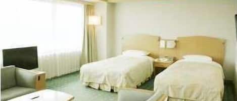 A hotel room with two beds, a desk, a chair, and a TV.