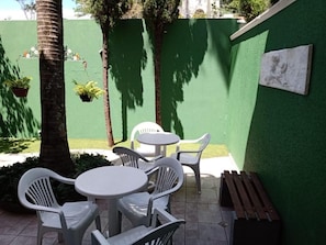 An outdoor patio with white plastic chairs and a round table, surrounded by green walls and potted plants. - Insta Hostel Floripa (Florianópolis)