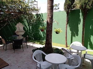 An outdoor patio area with a round table and chairs, surrounded by greenery and a green wall. - Insta Hostel Floripa (Florianópolis)