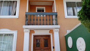 Un edificio con una puerta doble de madera, un balcón con barandilla de metal ornamentada y dos esculturas de piedra en la pared.