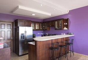 A kitchen with a central island, bar stools, and a stainless steel refrigerator.