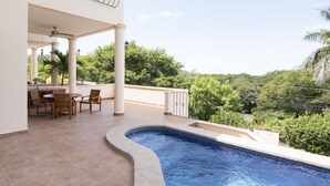 Une piscine à bord incurvé, entourée d’un patio couvert avec des chaises et une table.