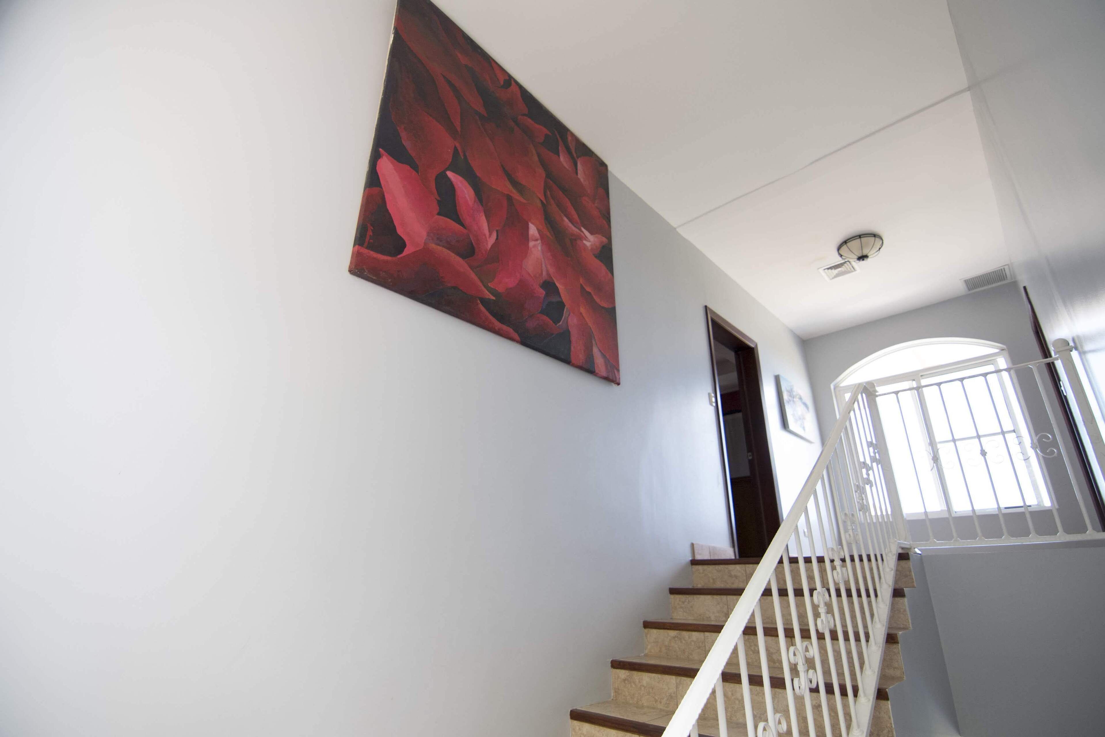 A staircase with a white railing, a red abstract painting on the wall, and a door at the top.