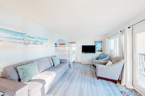 Relax in this inviting living area with a sofa, armchair, and TV, surrounded by a coastal theme and natural light.