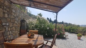 An outdoor patio with a stone wall, wooden table and chairs, a basket of flowers, and potted plants. - App.in semi-detached villa private garden and parking shared pool (Imperia)