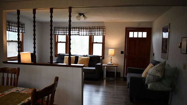 A cozy living room with a sofa, a dining table with chairs, a small side table, and a wooden floor. - Brook Road Condo (Goshen)