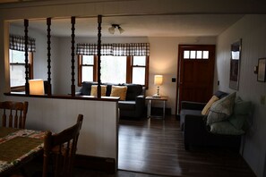 Ein gemütliches Wohnzimmer mit einer Couch, einem Esstisch mit Stühlen, einem kleinen Beistelltisch und Holzboden.