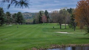 A golf course with a pond, trees, and a hilly landscape in the background. - Brook Road Condo (Goshen)