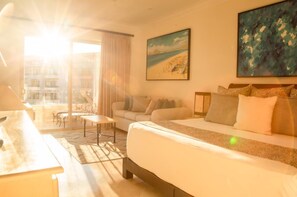 A hotel room with a bed, a sofa, a small table, and a painting of a beach scene.