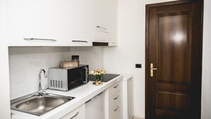 A kitchen with white cabinets, a stainless steel sink, a microwave, and a wooden door. - St. Peter's Heart -honeymoon luxury apartment Rome (roma)