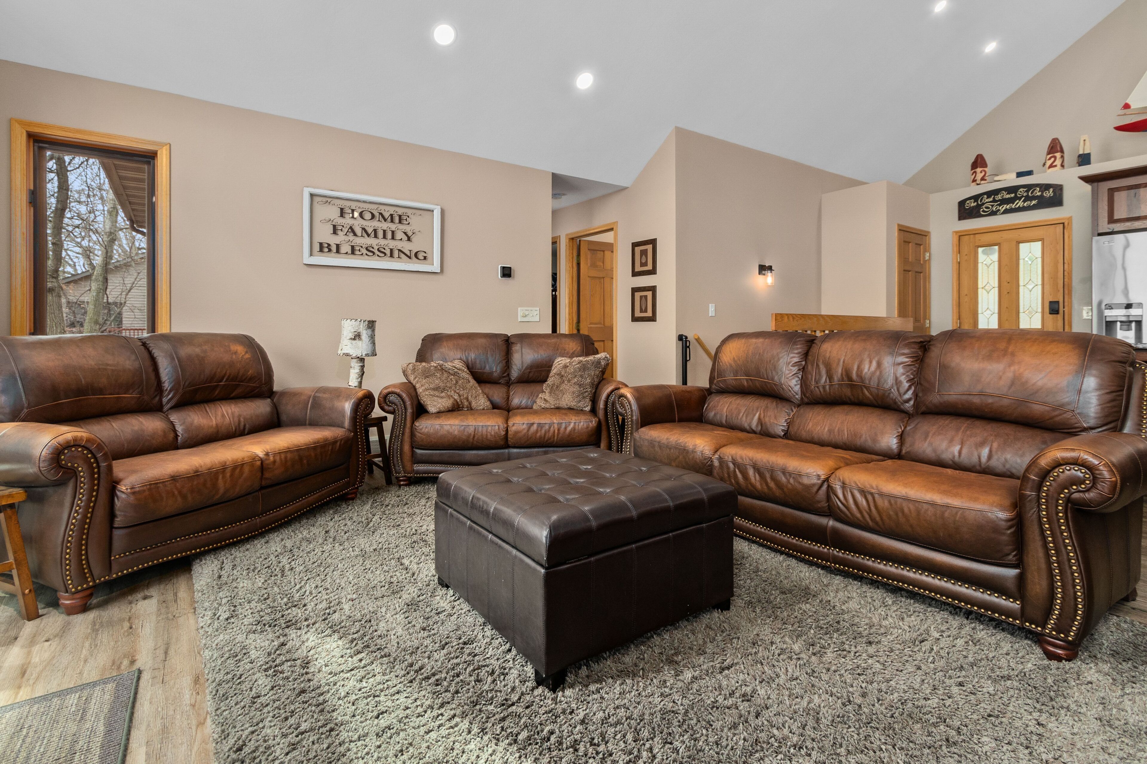 A spacious living room with two brown leather sofas, a matching ottoman, and a large rug.