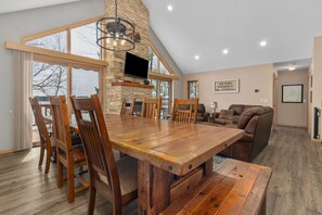 A spacious dining area with a large wooden table and chairs, a stone fireplace, and a television mounted on the wall. - Full Rec Lake w/pontoon to rent! 🏖 Beach. 🐶 friendly. (Wautoma)