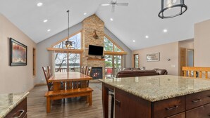 A spacious kitchen with a large island, wooden dining table, and a stone fireplace. - Full Rec Lake w/pontoon to rent! 🏖 Beach. 🐶 friendly. (Wautoma)