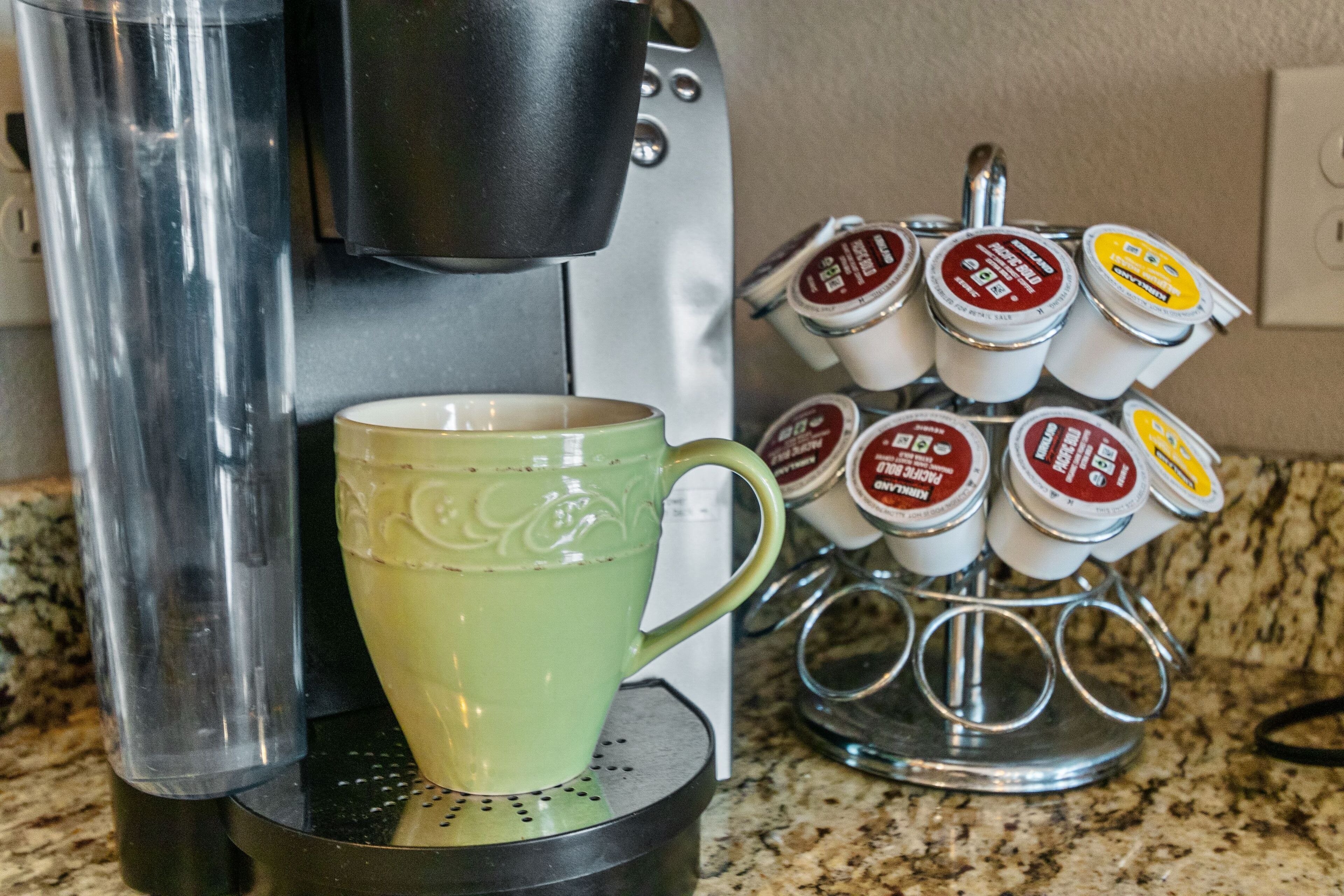 Una cafetera con bandeja de goteo, una taza verde y un soporte para cápsulas de café con varias cápsulas.