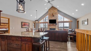 A spacious kitchen with a large island, wooden cabinets, and a stone fireplace. - Full Rec Lake w/pontoon to rent! 🏖 Beach. 🐶 friendly. (Wautoma)