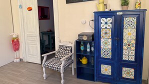 A room with a white door, a chair, a blue cabinet with decorative tiles, a painting of a sunset, and a small potted plant.