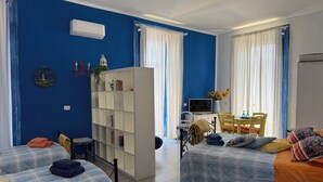 A room with two beds, a white bookshelf, a desk with a computer, and a dining area.