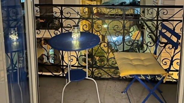 A balcony with a table and chairs, a view of buildings, and a glass door.