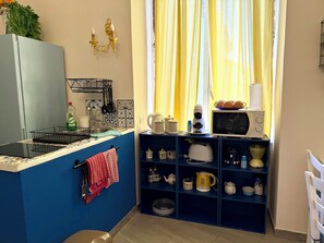 A compact kitchen with a blue countertop, a microwave, and a shelf with kitchenware.