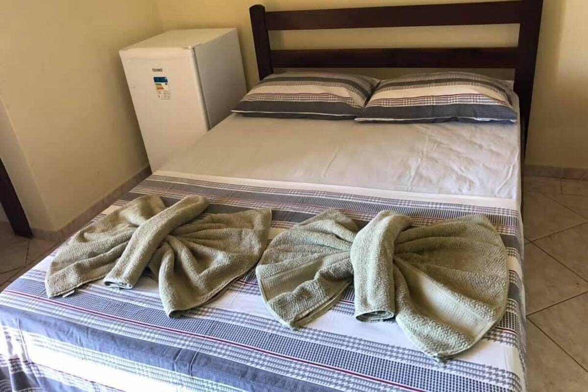 A hotel room with a bed, two pillows, a small white appliance, and two towels on the bed.