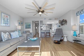 A living room with a sofa, coffee table, and a ceiling fan. There is a kitchen in the background with a bar area. - Stunning Ocean Views From Your Private Balcony, 613 New Haven Court (Fripp Island)