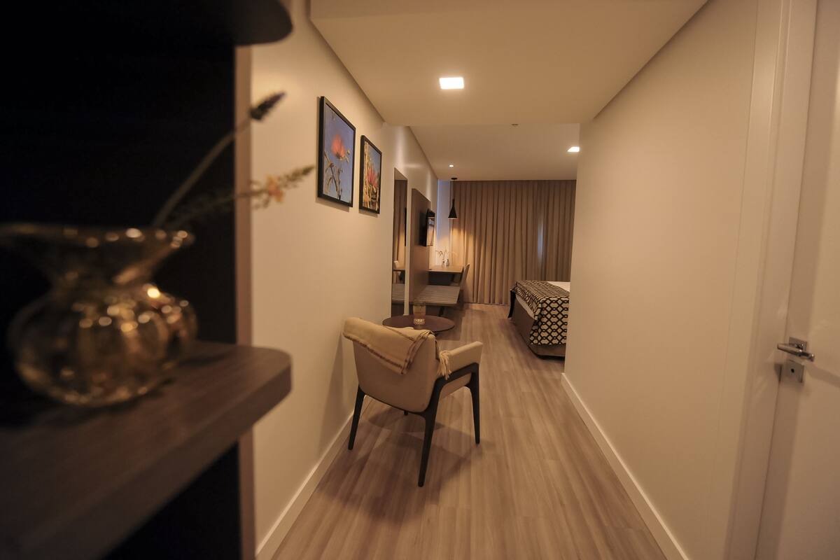 Un pasillo con una silla, una mesa y una lámpara. En la pared hay cuadros enmarcados y una puerta al final.