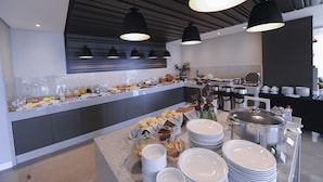 A buffet setup with various food items and beverages, a coffee station, and a buffet counter with plates and bowls. - Figueiras Hotel & Eventos (Sao Miguel Do Oeste)