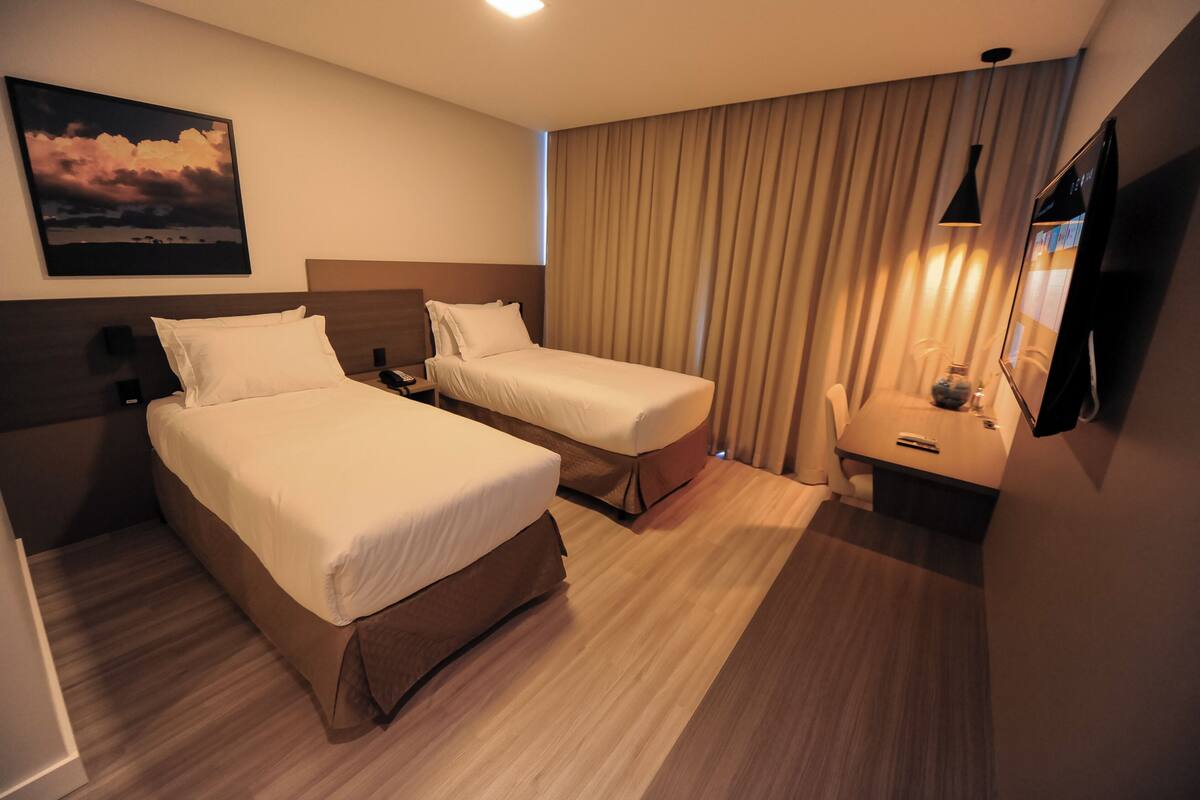 Una habitación de hotel con dos camas, televisión, escritorio y un cuadro en la pared.